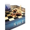Pudełko z napisem "5 in 1 WOODEN GAMES" zawiera drewnianą szachownicę z rozstawionymi pionkami w dwóch kolorach. Na szachownicy leży kilka przewróconych figur, a w tle widać metalowe wieczko pudełka.