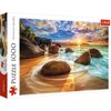Pudełko puzzli przedstawia krajobraz plaży z dużymi kamieniami, falami oceanu i zachodzącym słońcem na horyzoncie. Na opakowaniu widnieje napis "Puzzle 1000" oraz logo "Trefl".