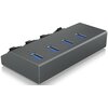 Na zdjęciu znajduje się czarny hub USB z czterema portami USB, każdy z niebieskim wnętrzem, oraz czterema przełącznikami na górnej powierzchni. Produkt ma prostokątny kształt i matowe wykończenie.
