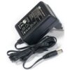 Czarny zasilacz z widocznymi oznaczeniami i specyfikacjami, takimi jak "AC/DC ADAPTER", "MODEL: S018CM1200200", "INPUT: 100-240V~50/60Hz 0.5A", "OUTPUT: 12V 2.0A", oraz różnymi symbolami certyfikacyjnymi. Zasilacz ma długi kabel zakończony wtykiem cylindr