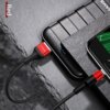 Czerwony kabel USB-Micro USB marki USAMS jest podłączony do smartfona i powerbanku, które leżą na ciemnej, kamiennej powierzchni. Na zdjęciu widoczny jest napis "USAMS" na wtyczce oraz słowo "Red" w lewym górnym rogu.