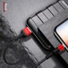Czerwony kabel USB-Lightning marki USAMS U5 o długości 1,2 m jest podłączony do smartfona i powerbanku, które leżą na ciemnej, kamiennej powierzchni. Na zdjęciu widoczny jest napis "USAMS" na wtyczce oraz słowo "Red" w lewym górnym rogu.