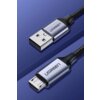 Na zdjęciu widoczny jest szary kabel USB - Micro USB z plecionym oplotem, z metalowymi końcówkami, na których znajduje się logo "UGREEN". Kabel leży na niebieskim tle, a jego końcówki są skierowane w przeciwnych kierunkach.
