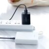 Czarny kabel USB - Micro USB UGREEN US289 o długości 0.5 m jest podłączony do czarnej ładowarki z logo "UGREEN", która znajduje się w białej listwie zasilającej. Na pierwszym planie widoczny jest biały power bank z logo "UGREEN".