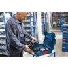 Mężczyzna w roboczym ubraniu trzyma otwartą walizkę narzędziową BOSCH L-Boxx 374, w której znajdują się narzędzia elektryczne. W tle widoczne są regały z innymi walizkami i narzędziami w magazynie.