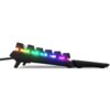 Na zdjęciu widoczna jest klawiatura z podświetleniem RGB, ukazana z profilu, z wyraźnie widocznymi kolorowymi światłami pod klawiszami. Klawiatura ma czarną obudowę i jest lekko uniesiona na nóżkach.