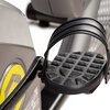 Zbliżenie na pedał roweru magnetycznego z wyraźnym bieżnikiem i paskiem zabezpieczającym. W tle widoczny jest fragment obudowy z żółtym okrągłym elementem.