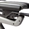 Zbliżenie na mechanizm regulacji siedziska roweru magnetycznego, z widocznymi śrubami i metalowym uchwytem. Siedzisko pokryte jest materiałem w kolorze szarym z czarnymi elementami.
