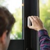 Na zdjęciu widać rękę montującą biały czujnik na ramie okna. Na czujniku widoczny jest napis "NETATMO".