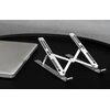 Na zdjęciu znajduje się metalowa podstawka pod laptopa z regulowanymi ramionami, ustawiona na ciemnej powierzchni obok zamkniętego laptopa. Produkt ma minimalistyczny design z otworami w ramionach, co nadaje mu lekkości.