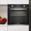 Czarny piekarnik elektryczny w zabudowie z widocznym panelem sterowania, na którym znajduje się wyświetlacz z liczbą "00:34" oraz pokrętła z oznaczeniami temperatury i funkcji. Obok piekarnika stoi misa z czerwonymi jabłkami.