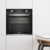 Czarny piekarnik elektryczny wbudowany w białą zabudowę kuchenną, z widocznym logo "beko" na dole drzwi. Na panelu sterowania znajdują się dwa pokrętła oraz wyświetlacz z czasem "00:34".
