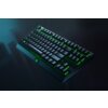 Na zdjęciu widoczna jest klawiatura mechaniczna z podświetleniem w kolorze zielonym, z logo Razer na dolnej części obudowy. Klawisze są wyraźnie widoczne, a całość utrzymana jest w ciemnej kolorystyce.