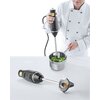 Na zdjęciu widoczny jest blender ręczny używany do miksowania brokułów w metalowym garnku, a obok leży drugi blender z widocznym ostrzem. Osoba obsługująca blender jest ubrana w biały strój kucharski.