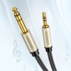 Na zdjęciu widoczny jest kabel audio z dwoma wtykami: większym 6.35 mm i mniejszym 3.5 mm, oba w kolorze złotym z metalicznymi obudowami, na których widnieje napis "UGREEN". Tło jest jasne z delikatnymi motywami muzycznymi, takimi jak nuty.