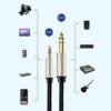 Na zdjęciu znajduje się kabel audio z dwoma wtykami: 3.5 mm i 6.35 mm, z widocznym logo "UGREEN" na obu końcówkach. Wokół kabla przedstawione są różne urządzenia elektroniczne, takie jak komputer, laptop, smartfon, głośnik, mikser i gitara, z oznaczeniami