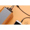 Na zdjęciu widoczny jest drewniany głośnik z podłączonym kablem Jack 3.5 mm - 2x RCA marki UGREEN, który łączy się z telefonem. Obok telefonu leżą suszone kwiaty na pomarańczowym tle.