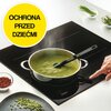Na zdjęciu znajduje się płyta indukcyjna z garnkiem pełnym zielonej zupy, nad którym unosi się para, a obok widoczna jest dłoń wskazująca na panel sterowania. W lewym górnym rogu znajduje się żółte koło z napisem "OCHRONA PRZED DZIEĆMI", a na płycie widoc