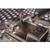 Na zdjęciu widoczny jest metalowy element mocowany w imadle, obrabiany frezem GRAPHITE 55H363. Tło składa się z metalowej kratki, a frez jest zamocowany w narzędziu elektrycznym.