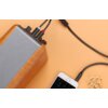 Na zdjęciu widoczny jest czarny kabel Jack 3.5 mm - 2x RCA marki UGREEN o długości 0.25 m, podłączony do urządzenia audio oraz smartfona na jasnym tle. Obok smartfona znajdują się suszone kwiaty.