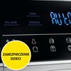 Zbliżenie na panel sterowania suszarki z wyświetlaczem pokazującym cyfry oraz przyciskami oznaczonymi jako "Dry Level", "Delay" i "Childlock". Na dole widoczny jest żółty okrąg z napisem "ZABEZPIECZENIE DZIECI".