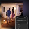 Na zdjęciu widać oświetlony ganek domu z zamontowaną lampą ścienną oraz fragment ekranu smartfona z aplikacją, na którym widnieje tekst: "Add outdoor sensor. You successfully connected the Hue Outdoor Sensor. Please select the room where this sensor will 
