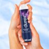 Na zdjęciu widoczny jest niebieski produkt z napisem "durex PERFECT GLISS ŻEL INTYMNY SILIKONOWY 50 ml" trzymany w dłoniach. Tło jest rozmyte i ma jasnoniebieski kolor.