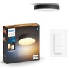 Na zdjęciu znajduje się czarna lampa sufitowa oraz pudełko z napisem "PHILIPS hue White ambiance Enrave S ceiling light" i hasłem "Personalize your home with smart lighting". Obok widoczny jest biały pilot z trzema przyciskami, w tym jednym z symbolem włą
