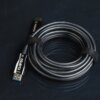 Na zdjęciu widoczny jest zwinięty czarny kabel HDMI z oznaczeniem "CLAROC" oraz "Source" na jednym z końców. Kabel jest spięty czarnym rzepem, a na wtyczce znajduje się napis "HDMI".