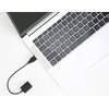 Na zdjęciu widoczny jest srebrny laptop z czarną klawiaturą, do którego podłączony jest czarny adapter audio przez port USB. Adapter ma dwa wejścia jack 3.5 mm i leży na białej powierzchni.