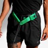 Czarna saszetka z zielonym paskiem i klamrą, na której widnieje napis "ZEE RUN". Produkt noszony jest na czarnych szortach z widocznym logo "TRACK & FIELD".