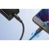 Czarny kabel USB - Micro USB jest podłączony do smartfona i ładowarki, z widocznym logo "UGREEN" na wtyczce. Tło jest jasnoniebieskie, a wokół kabla widoczne są niebieskie symbole błyskawic.