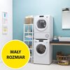 Na zdjęciu znajduje się biała suszarka ustawiona na pralce w jasnym pomieszczeniu z niebieską ścianą, obok stoi regał z ręcznikami i koszykiem. W lewym dolnym rogu widoczny jest żółty okrąg z napisem "MAŁY ROZMIAR".