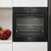 Czarny piekarnik elektryczny w zabudowie z widocznym logo "beko" na dole, z wyświetlaczem pokazującym czas 00:35 i temperaturę 230°C. Obok piekarnika stoi miska z czerwonymi jabłkami.