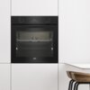 Czarny piekarnik elektryczny wbudowany w białą zabudowę kuchenną, z widocznym logo "beko" na dole drzwi. Na panelu sterowania wyświetla się czas "00:34", a po obu stronach znajdują się pokrętła.