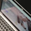 Na zdjęciu widoczny jest ekran laptopa z zaślepką kamery oznaczoną logo "Savio". Na ekranie wyświetlana jest rozmyta strona internetowa z widocznymi elementami interfejsu.