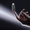Na zdjęciu widoczny jest adapter USB z napisem "UGREEN" trzymany na palcu, oświetlony jasnym światłem na ciemnym tle. Adapter ma kompaktowy, metaliczny wygląd z niebieską diodą.