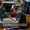 Na zdjęciu widoczna jest osoba siedząca na ławce, nosząca słuchawki nauszne i patrząca na telefon. Na zdjęciu znajduje się tekst: "WH-1000X M5" oraz "Spersonalizuj swój dźwięk w aplikacji. Użyj Fast Pair/Swift Pair dla łatwego parowania."