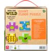 Na zdjęciu znajduje się opakowanie puzzli "Into the Wild Giant Floor Puzzle" z 26 dużymi, dwustronnymi elementami, przedstawiające litery i cyfry z ilustracjami zwierząt. Widoczne są cztery przykładowe elementy z literami U i E oraz cyframi 4 i 14, a takż