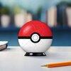 Na zdjęciu znajduje się trójwymiarowa kula złożona z puzzli, przypominająca wyglądem Pokéball, z charakterystycznym czerwono-białym wzorem i czarnym paskiem z okręgiem pośrodku. Kula stoi na czarnej podstawce, a obok niej leży żółty ołówek na białej powie