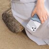 Osoba trzyma telefon w etui o abstrakcyjnym wzorze w odcieniach niebieskiego, białego i szarego. Tło zdjęcia stanowi piasek oraz fragment jasnego materiału.