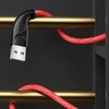Czerwony, pleciony kabel USB z wtyczką USB na jednym końcu jest owinięty wokół dwóch złotych prętów na ciemnym tle. Na czarnej obudowie wtyczki widoczne jest logo w kształcie litery "n".