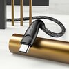 Na zdjęciu widoczny jest pleciony kabel USB-C z czarną końcówką, na której znajduje się napis "USAMS". Kabel leży na złotym cylindrze, a w tle widać elementy dekoracyjne w kolorze złotym i szarym.