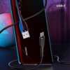 Na zdjęciu widoczny jest czarny kabel USB - USB-C podłączony do smartfona z napisem "HUAWEI", a w tle znajduje się tekst "USB-C". Kabel ma metaliczne wykończenie, a scena jest oświetlona kolorowymi światłami.