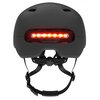 Czarny kask z widoczną czerwoną lampką LED z tyłu, posiada regulowane paski i mechanizm dopasowujący. Na lampce znajdują się dwa przyciski z symbolami strzałek.