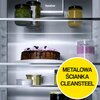 Wnętrze lodówki z metalową ścianką, na której widnieje napis "DynaCool". Na półkach znajdują się słoiki z przetworami, tort z różowymi dekoracjami oraz napis na żółtym tle: "METALOWA ŚCIANKA CLEANSTEEL".