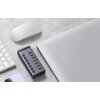 Na zdjęciu znajduje się hub UGREEN z siedmioma portami USB i przyciskami, obok klawiatury, myszki i laptopa na szarej powierzchni. Na hubie widoczne jest logo "UGREEN".