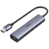 Na zdjęciu znajduje się adapter USB w kolorze szarym z czterema portami USB i jednym portem micro USB, z logo "UGREEN" na górnej powierzchni. Adapter jest połączony z kablem USB, który ma plecioną osłonę.