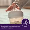Na zdjęciu widoczna jest butelka z napisem "PHILIPS AVENT", trzymana przez dziecko. Na dole zdjęcia znajduje się tekst: "Dziecko ssie, przełyka i oddycha we własnym rytmie" oraz ikona smoczka na fioletowym tle.