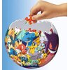 Na zdjęciu widać kuliste puzzle 3D z motywem postaci z serii Pokemon, które są w trakcie składania. Ręka trzymająca pomarańczowy element puzzli znajduje się nad niemal ukończoną kulą, na której widoczne są różnokolorowe postacie.
